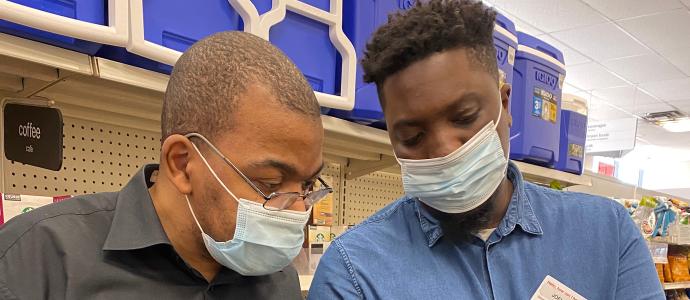 Shakkar at work with a colleague in CVS. They both wear masks and are looking at an item