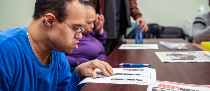 Several people are sat at a table reading newspaper articles.