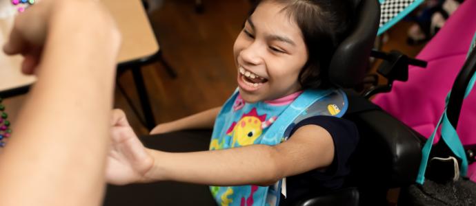 iHOPE student is smiling excitedly as she reaches out to an arm offering mardi gras beads, she's in a wheelchair