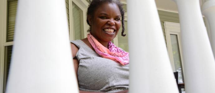 Looking through outdoor railing you can see someone sitting, looking, and smiling at the camera