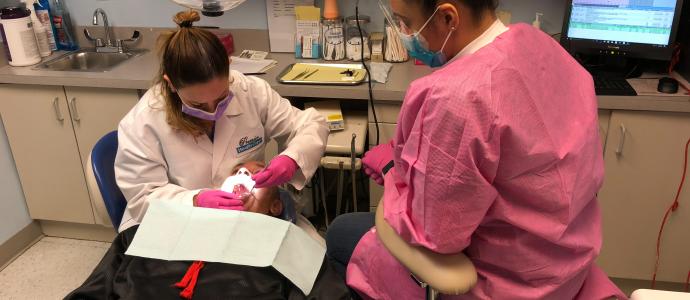 Person in a dental chair while dentist and assistant work on their teeth