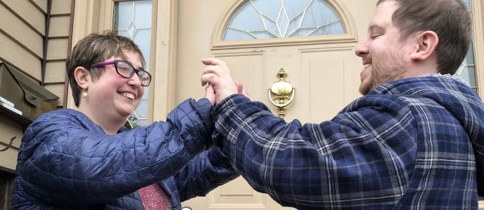 Two people stand outside an NIPD/NJ residence, they face each other and each has both hands up and palms against each other