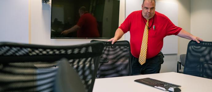 Person in red shirt is moving chairs under the table in a conference room.