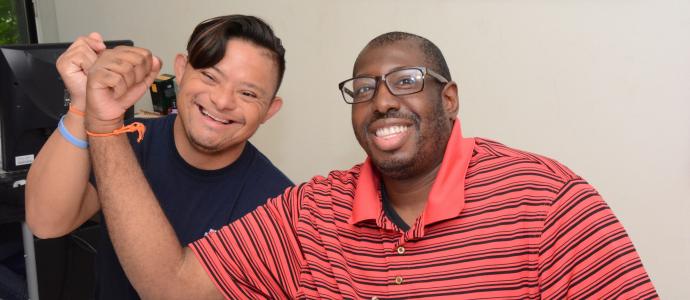 Two people sat together at a table, they have their arms up together with closed fist. they are both smiling