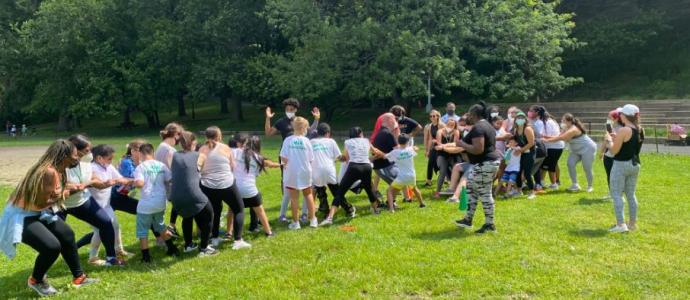 Large group of people outside on lush green grass, they appear to be playing "tug of war"