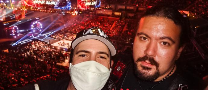 Richard and Luis stand together at the All Elite Wrestling show in Flushing. One wears a mask. There is a big crowd and a wrestling ring in the background