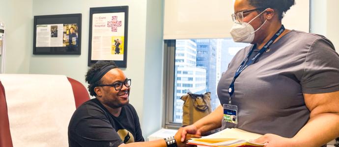 Darren sits in a doctors office and shakes hands with a person wearing a mask and scrubs, holding a manila folder