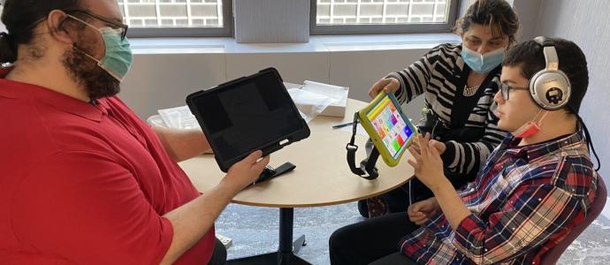 3 people sit around a table with a large ipad and a small one.