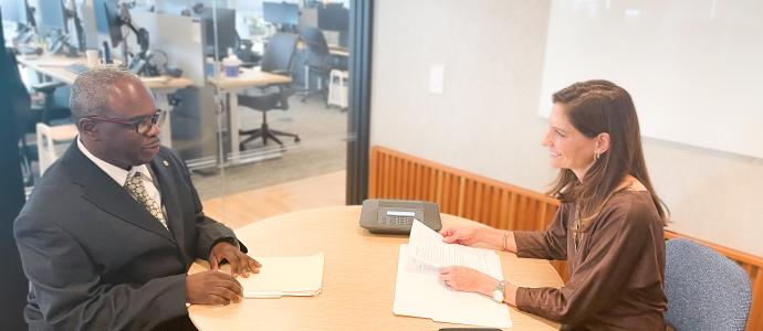 Two people sit at an office table practicing interview skills