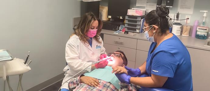 Kelvin is in the dental chair, fully reclined as the dentist cleans his teeth, he is holding hands with another clinician who sits on the other side of him