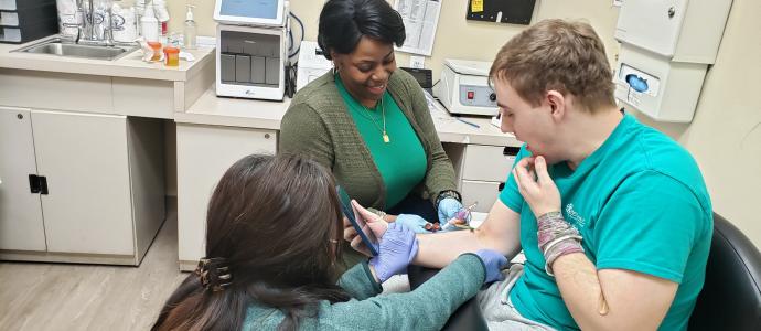 Patient at Premier HealthCare getting blood drawn with a nurse and OT supporting him.