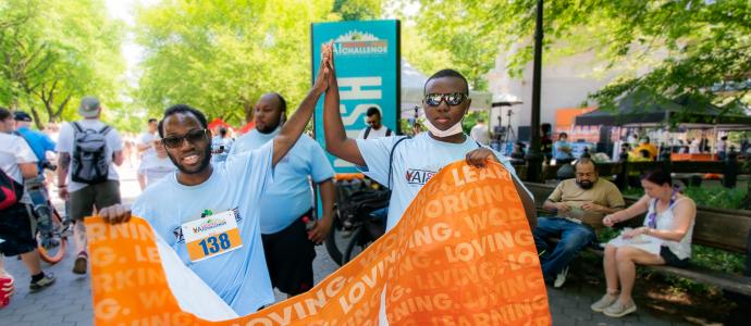 Diogeneis and a friend high-five each other while holding the CPC banner at the Central Park Challenge