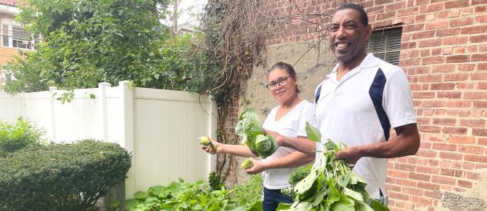 Two staff stand in Riverside Garden holding some of the veggies they've grown