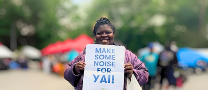Destiny stands in Central Park holding a sign that says "Make some noise for YAI"