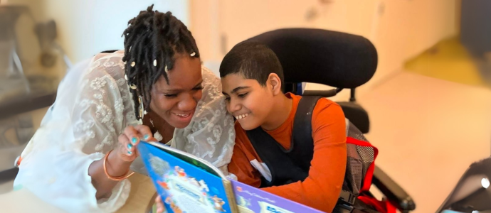 Paraprofessional reads to a student who is in a wheelchair, they are both smiling