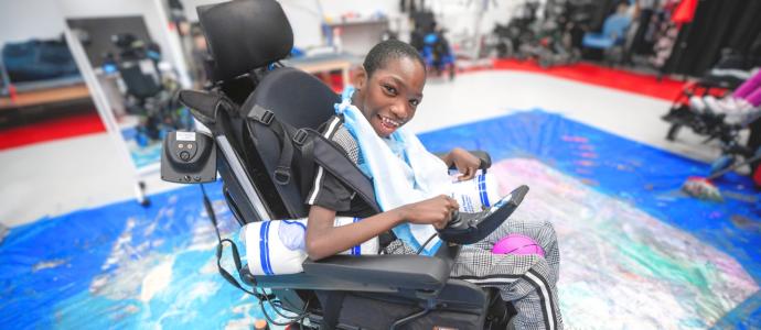 young student in his powerchair in the middle of some powerchair art on the ground. He looks very proud.