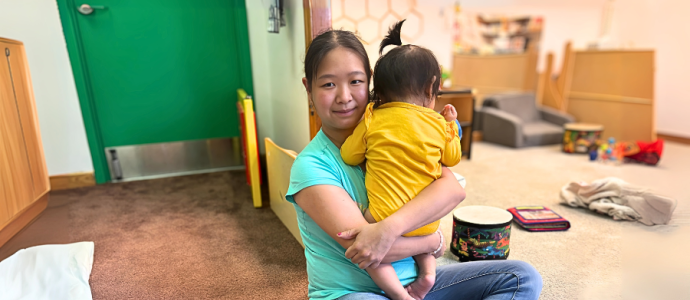 Mei-Feng sits cross legged on the floor of daycare while holding a baby