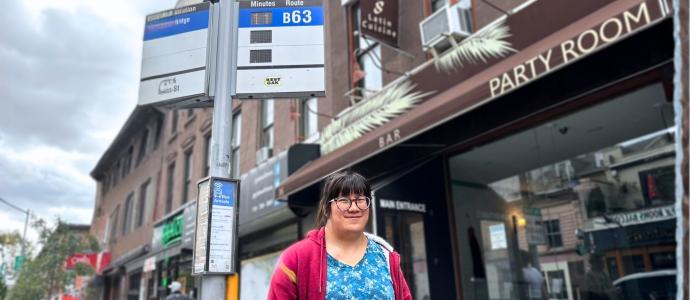 Lily stands at a bus stop in Brooklyn