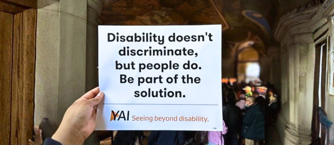 Someone holds up a rally sign "Disability doesn't discriminate, but people do. Be part of the solution."