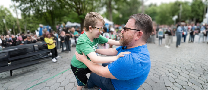 Adult is holding a child in Central Park, they are both looking at each other and appear to be happy