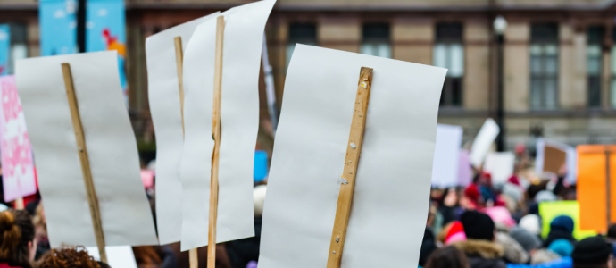 the back of 3 signs (no writing visible) at a protest