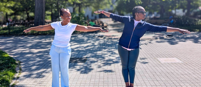 Two woman stand in a park with their arms out stretching