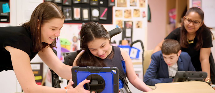 classroom setting at iHOPE with two students supported by staff are looking at screens