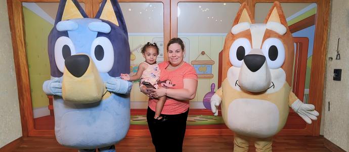 Elizabeth stands holding her daughter on her hip between Bluey and Bingo
