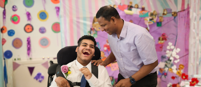Man stands looking over a student in a wheelchair at prom. They are both smiling big smiles