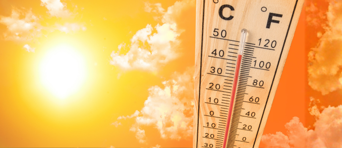 Close-up of a mercury thermometer marked with C and F scales, with a red liquid line, set against a bright orange-yellow sky with scattered clouds.