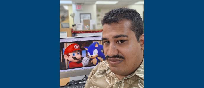 Orland sitting at a desk looking at a computer screen showing Mario and Sonic character artwork in an office.