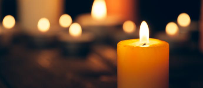 A burning candle in foreground with blurred burning candles behind it in on a black background