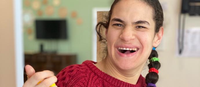 Heather wears a red sweater, has her right hand up, and is smiling