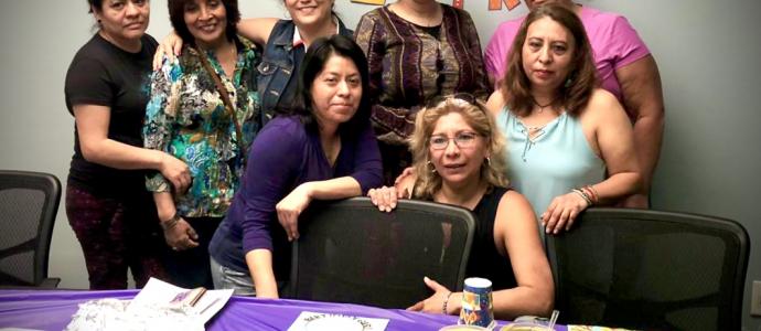 Group of people stand in front of bunting flags on wall and a table with food and a purple table cloth