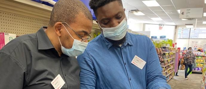 Portrait of Shakar Hollins (left) with a colleague (right) at CVS they are wearing disposable face masks and looking at an item