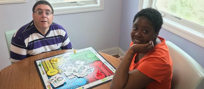 two people sit at a table, they are looking at the camera, the game "Sorry" is at the table.