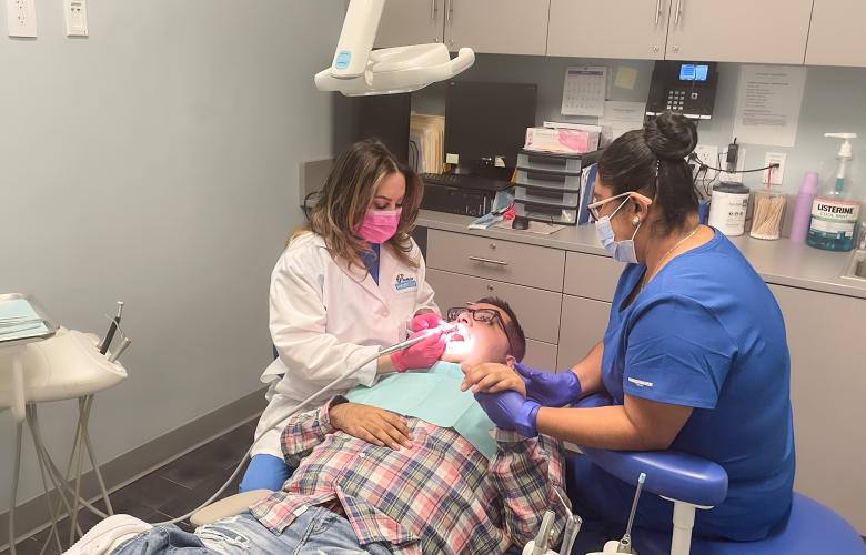 Kelvin is in the dental chair, fully reclined as the dentist cleans his teeth, he is holding hands with another clinician who sits on the other side of him