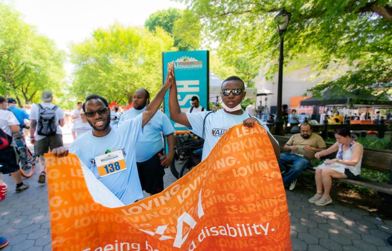 Diogeneis and a friend high-five each other while holding the CPC banner at the Central Park Challenge