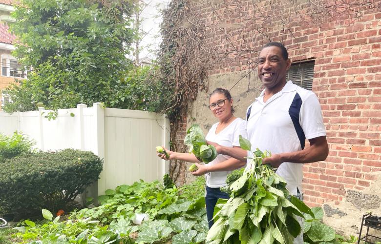 Two staff stand in Riverside Garden holding some of the veggies they've grown