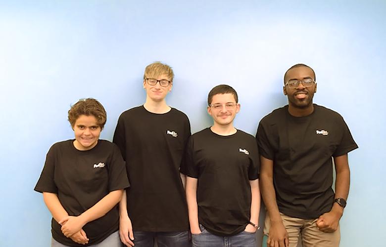 Group of 4 people stand leaning against a wall, all wearing black FedEx shirts and smiling for picture