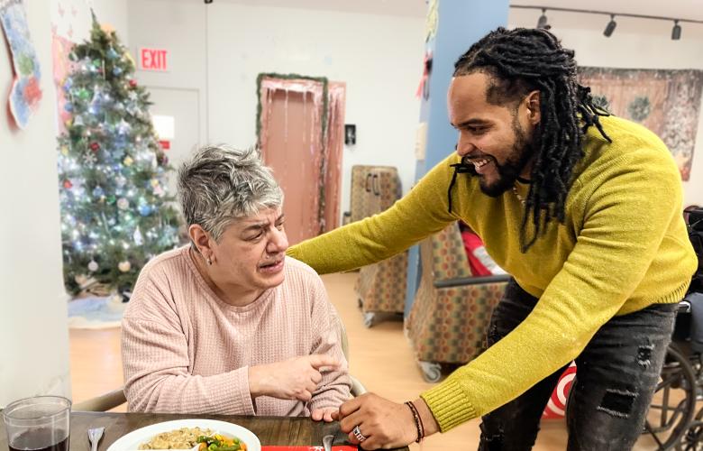 Jesse Paez crouches next to a YAI resident who is talking to him