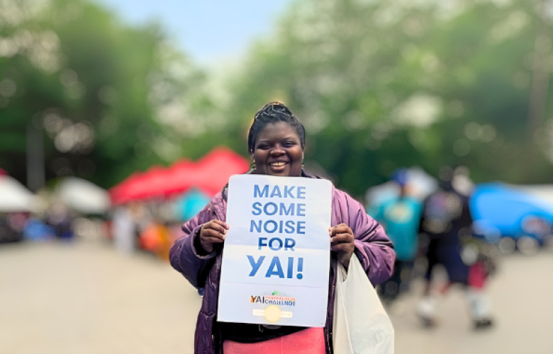 Destiny stands in Central Park holding a sign that says "Make some noise for YAI"