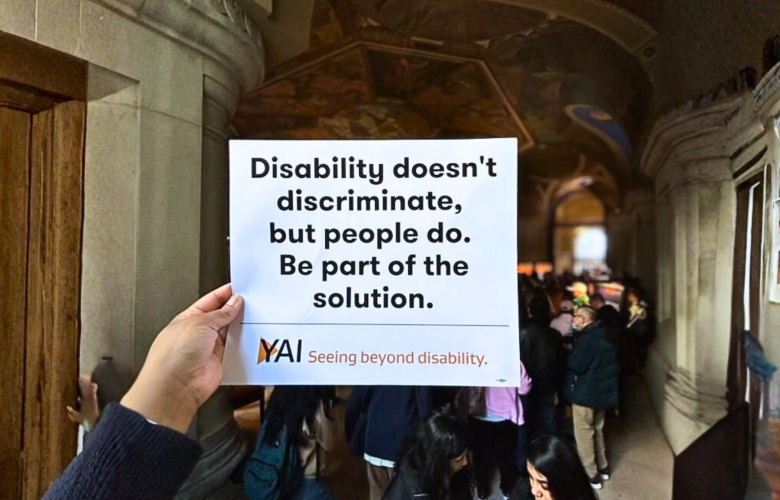 Someone holds up a rally sign "Disability doesn't discriminate, but people do. Be part of the solution."