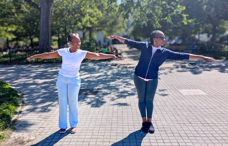 Two woman stand in a park with their arms out stretching