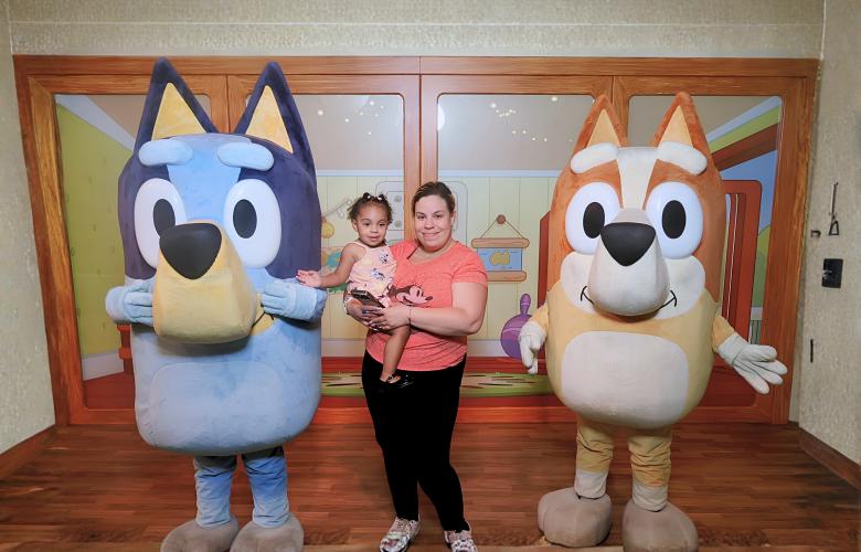 Elizabeth stands holding her daughter on her hip between Bluey and Bingo
