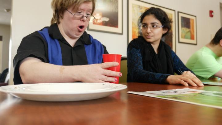 Two people sit at table, there's a plate in foreground, person on left holds a red cup