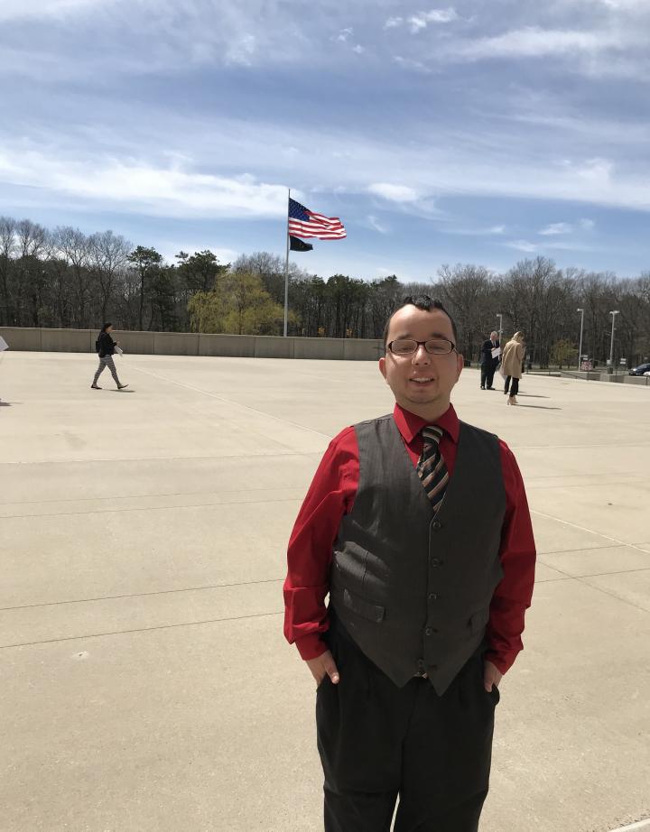 Alex stands outside, a US flag flies behind him