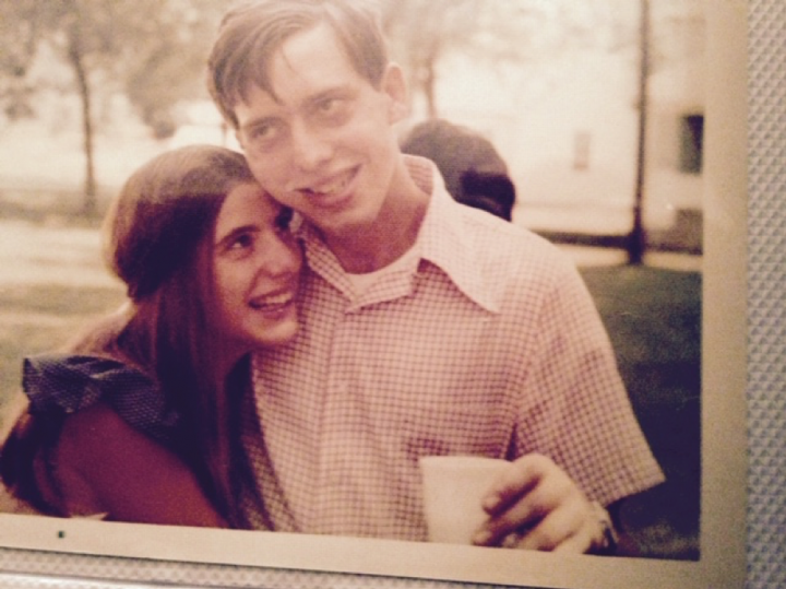 Older photo of a young man holding a cup with a young woman hugging him from the side