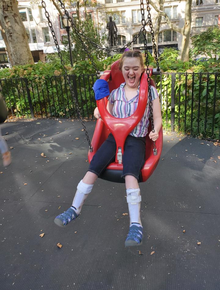 Amelia with a very big smile/laughter is in a red adaptive swing