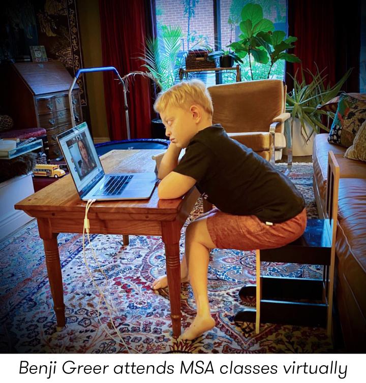 Benji sits at a table at home looking at a laptop